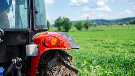 Close-up of red tractor rear with muddy tire and lights in green agricultural field