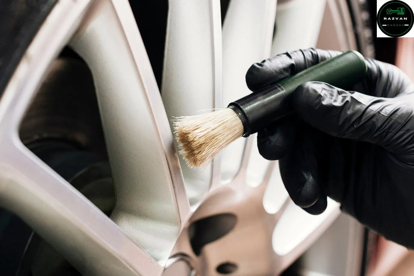 Gloved hand cleaning car alloy wheel with detailing brush for auto maintenance